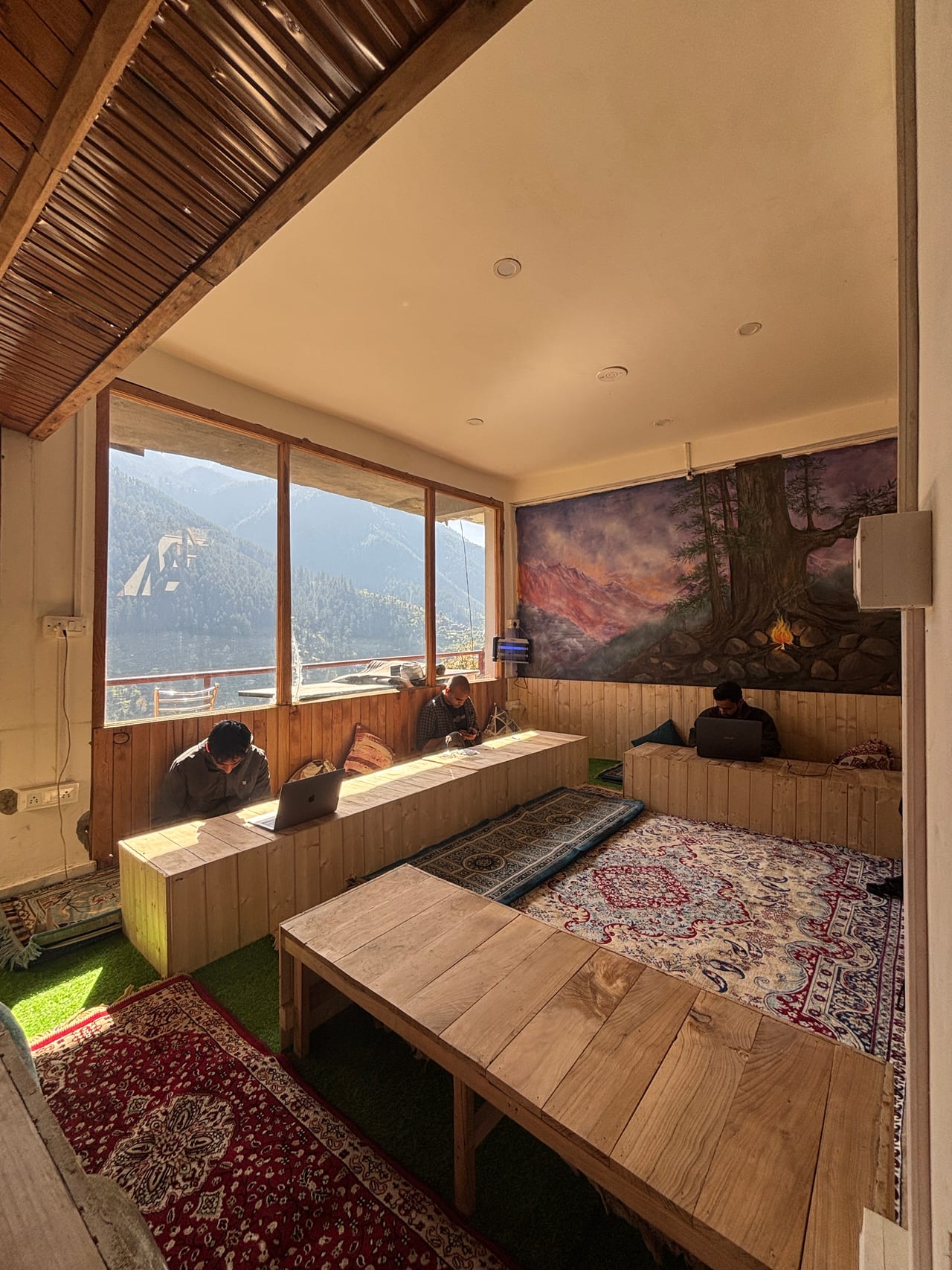 Emberwood rooftop café interior — wooden floors, Persian rugs, mountain view through tall windows